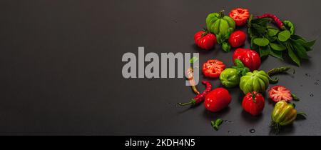 Grüne und rote gerippte Tomaten, amerikanische oder florentinische Sorte. Reifes Gemüse, Chili, frische Lorbeerblätter. Trendiges hartes Licht, dunkler Schatten, Steinbeton Stockfoto