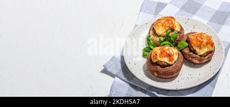 Gebackene gefüllte Pilzkappen bereit zum Essen. Champignons, Gewürze, Gemüse, Käse. Servierte Portion, trendiges hartes Licht, dunkler Schatten. Weißer Putz b Stockfoto