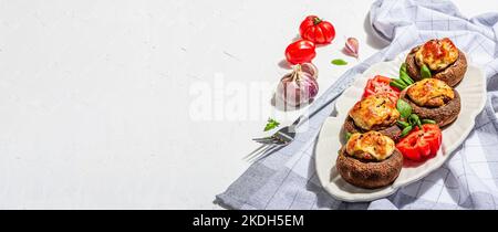 Gebackene gefüllte Pilzkappen bereit zum Essen. Champignons, Gewürze, Gemüse, Käse. Servierte Portion, trendiges hartes Licht, dunkler Schatten. Weißer Putz b Stockfoto