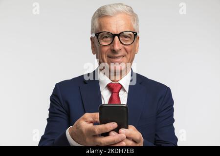 Geschäftsmann, der etwas am Telefon schrieb, während er der Kamera vor grauem Hintergrund das Lächeln auf den Lippen gab Stockfoto