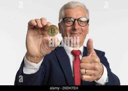Geschäftsmann, der einen Bitcoin hält und ein OK-Zeichen gibt, ermutigt, in Krypto-Münzen zu investieren Stockfoto