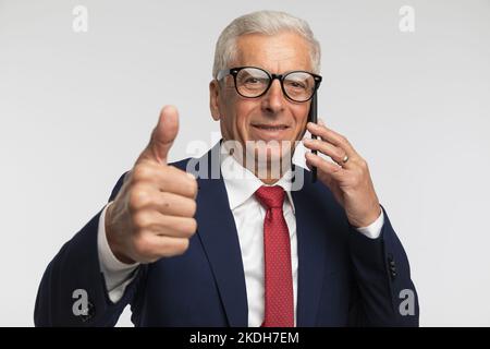 Geschäftsmann gab ein OK-Schild und zeigte, dass das Gespräch am Telefon vor grauem Studiohintergrund in Ordnung war Stockfoto