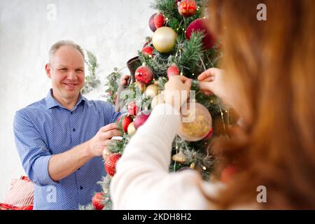 Lächelndes, glückliches Paar im mittleren Alter, das Weihnachtsbaum zu Hause schmückt. Glückliches Paar zusammen zu Hause, weihnachtskonzept Stockfoto