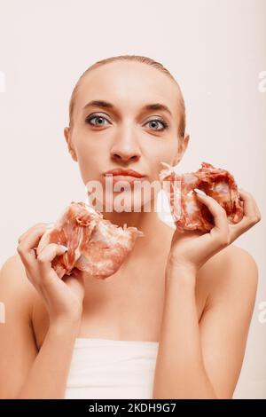 Ein junges Mädchen auf weißem Hintergrund hält rohes Fleisch in den Händen Stockfoto