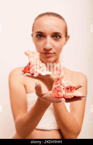 Ein junges Mädchen auf weißem Hintergrund hält rohes Fleisch in den Händen Stockfoto