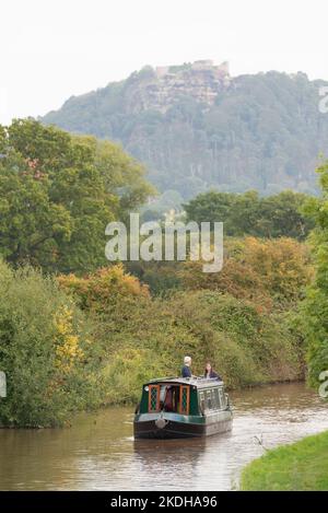 Ein Narrowboot, das im Herbst den Shropshire Union Canal mit den Rocky Crags of Beeston Castle, Ceshire, im Hintergrund befährt Stockfoto