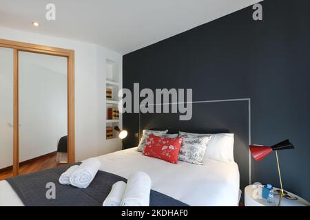 Modernes Schlafzimmer mit Doppelbett, schlichten dunkelblauen und weißen Wänden, Einbauschrank mit Spiegelschiebetüren Stockfoto