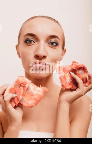 Ein junges Mädchen auf weißem Hintergrund hält rohes Fleisch in den Händen Stockfoto