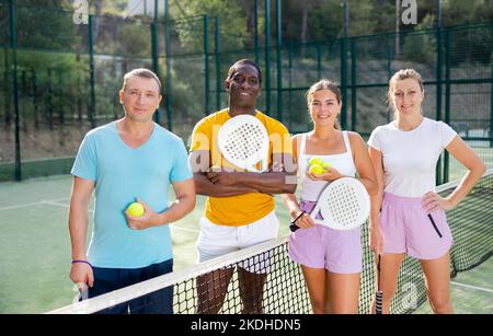 Fröhliche junge und Erwachsene Männer und Frauen paddeln Tennisspieler auf dem Platz Stockfoto