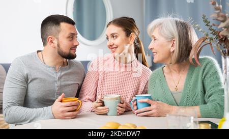 Porträt eines positiven jungen Paares und einer älteren Frau, die zu Hause Tee trinkt Stockfoto