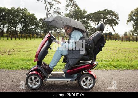 Rentnerin auf einem Motorroller draußen im Regen Stockfoto