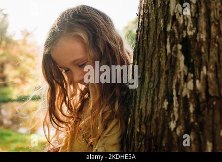 Nahaufnahme Porträt eines schönen Mädchen versteckt bei einem Baum in goldenem Licht Stockfoto