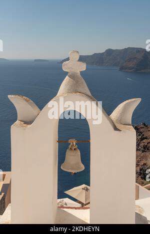 Oia, Santorini, Griechenland. 2022. Weißer Glockenturm mit Kreuz und einzelner Glocke mit Blick auf die Ägäis vom Dorf Oia, Santorini. Stockfoto