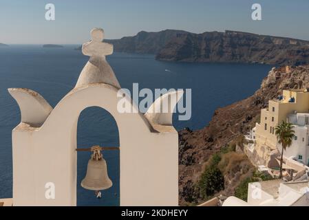 Oia, Santorini, Griechenland. 2022. Weißer Glockenturm mit Kreuz und einzelner Glocke mit Blick auf die Ägäis vom Dorf Oia, Santorini. Stockfoto