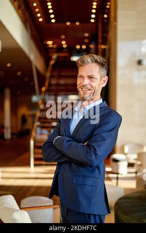 Porträt eines lächelnden Geschäftsmannes mit gekreuzten Armen am Arbeitsplatz Stockfoto