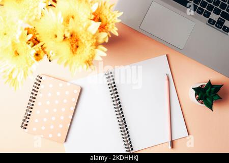 Rosa Desktop mit Notebook, Laptop-Computer, Bleistift, Strauß gelber Blumen und saftiger Pflanze. Draufsicht, flach liegend. Stockfoto