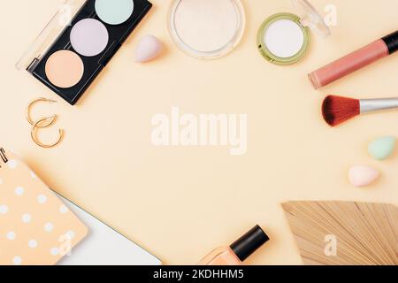 Rahmen aus Make-up und Accessoires mit Notizblock und Palmenblatt auf beigem Hintergrund. Draufsicht, flach liegend. Stockfoto