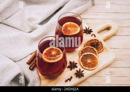 Zwei Gläser mit Glühwein auf Holzschneidebrett mit Gewürzen und Orangenscheiben, Draufsicht. Stockfoto