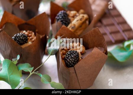 Schokoladen-Cupcake. Muffin mit Brombeeren und Eukalyptusblättern auf Silberfolie. Schokoladendessert. Süßer Tisch. Süßigkeiten und Desserts. Gebacken Stockfoto