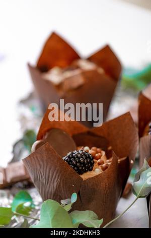 Schokoladendessert. Schokoladen-Cupcake. Muffin mit Brombeeren und Eukalyptusblättern auf Silberfolie. Süßer Tisch. Süßigkeiten und Desserts. Gebacken Stockfoto