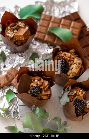 Schokoladen-Muffin mit Brombeeren und Eukalyptusblättern auf Silberfolie. Schokoladendessert. Süßigkeiten und Desserts. Backwaren und Desserts Stockfoto