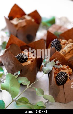 Backwaren und Desserts. Schokoladen-Cupcake. Muffin mit Brombeeren und Eukalyptusblättern auf Silberfolie. Schokoladendessert. Süßer Tisch Stockfoto