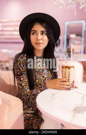 Gesicht einer jungen Frau im Hut, die Kaffee mit Stroh trinkt, erfrischendes Getränk, entspannter Lebensstil Stockfoto