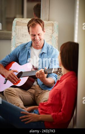 Musik ist eine andere Sprache der Liebe. Ein Mann, der zu Hause für seine Frau Gitarre spielt. Stockfoto