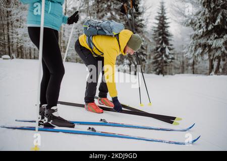 Seniorenpaar, das Ski anlegt und sich auf die Fahrt in der winterverschneiten Natur vorbereitet. Stockfoto