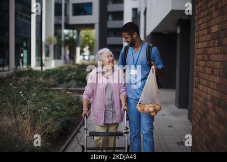 Glücklicher Betreuer, der mit seiner älteren Kundin aus dem Lebensmittelgeschäft zurückkehrte. Stockfoto