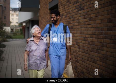 Glücklicher Betreuer, der mit seiner älteren Kundin aus dem Lebensmittelgeschäft zurückkehrte. Stockfoto