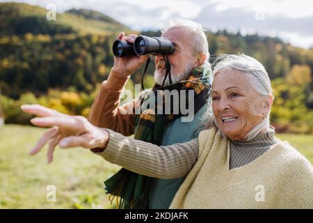 Ein älteres Paar, das beim Herbstspaziergang durch ein Fernglas die Aussicht betrachtet. Stockfoto