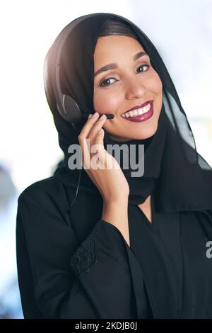 Das freundliche Gesicht auf der anderen Seite des Telefons. Porträt eines freundlichen jungen muslimischen Callcenters, der in einem modernen Büro arbeitet. Stockfoto