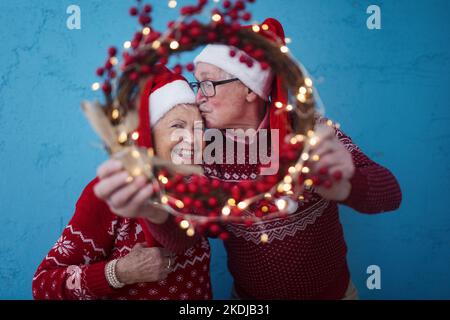 Porträt eines glücklichen älteren Paares mit Weihnachtsmann-Hüten im Studio, Blick durch den Weihnachtskranz. Stockfoto