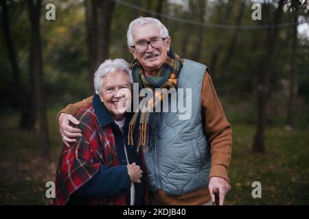 Porträt eines älteren Paares, das im Herbstwald zusammenläuft. Stockfoto