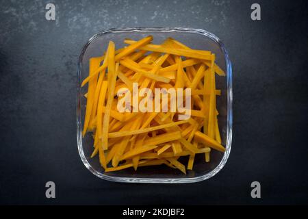 Frische geklischte Karotten in einer kleinen Glasschüssel auf dunkler Oberfläche Stockfoto