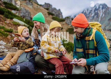 Glückliche Familie, die sich ausruhte, beim gemeinsamen Wandern in den herbstlichen Bergen einen Imbiss. Stockfoto