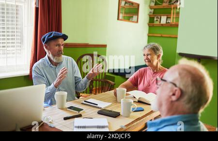 Hier sind meine Vorschläge. Drei Senioren, die sich zu Hause um einen Tisch treffen. Stockfoto