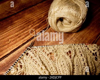 Prozess des Strickens. Stricknadeln, Schlaufen auf Stricknadeln, Strickstoff, Fadenknäuel, grobes Baumwoll- und Leinengarn, Holzhintergrund Stockfoto