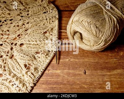 Durchbrochene Tischdecke beim Stricken. Stricknadeln, Schlaufen auf Stricknadeln, Strickstoff, Fadenknäuel, grobe Baumwolle und Leinen Stockfoto