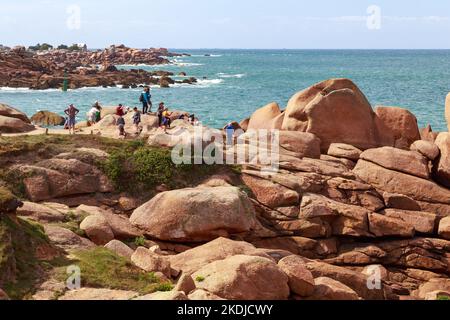 PLOUMANACH, FRANKREICH - 5. SEPTEMBER 2019: Es handelt sich um eine Gruppe von Menschen auf den ungewöhnlich farbigen Granitfelsen an der rosafarbenen Granitküste in der Bretagne. Stockfoto
