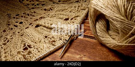 Durchbrochene Tischdecke beim Stricken. Stricknadeln, Schlaufen auf Stricknadeln, Strickstoff, Fadenknäuel, grobe Baumwolle und Leinen Stockfoto