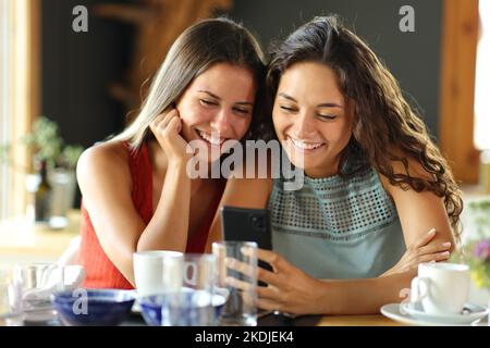 Vorderansicht von zwei glücklichen Freunden, die in einem Restaurant einen schicken Pone checken Stockfoto
