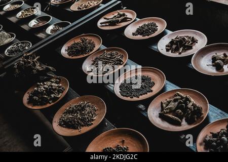 Verschiedene Gewürze auf kleinen Keramik- und Metallplatten auf schwarzem Holzhintergrund displaced Stockfoto