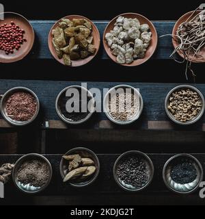 Verschiedene Gewürze auf kleinen Keramik- und Metallplatten auf schwarzem Holzhintergrund displaced Stockfoto