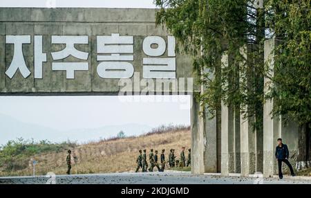 Panmunjom, Nordkorea. 17. Oktober 2016. Soldaten sahen unter einem Propagandagemälde gehen, das sagte: „Lasst uns ein vereintes Mutterland übergeben!“ Am Eingang von Panmunjom von der nordkoreanischen Seite. Das Waffenstillstandsdorf Panmunjom innerhalb der entmilitarisierten Zone (DMZ) trennt Nord- und Südkorea seit 1953. Die militärische Demarkationslinie ist von Nordkoreas Seite aus zu sehen. (Bild: © Jasmine Leung/SOPA Images via ZUMA Press Wire) Stockfoto