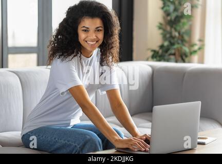 Junge afroamerikanische Frau schaut auf die Kamera und lächelt. Studentin oder Freiberuflerin, die arbeitet Stockfoto