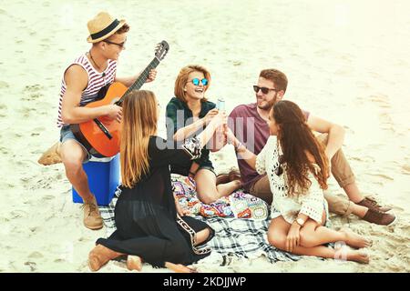 Ein junger Mann spielt Gitarre für seine Freunde, während er am Strand chillte. Stockfoto