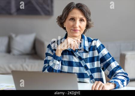 Erfolgreiche seriöse Geschäftsfrau, die am Arbeitsplatz im modernen Büro oder zu Hause sitzt Stockfoto