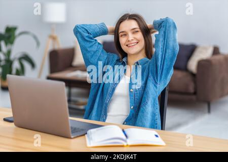 Junge Büroangestellte oder Freiberuflerin, die die Hände hinter dem Kopf hält, Pause macht, sich entspannt, an etwas denkt Stockfoto